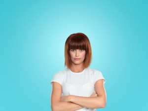 Woman stands with her arms folded against a blue background