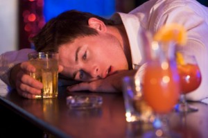 Man with head on bar surrounded by drinks