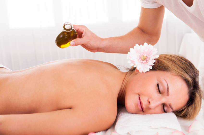 Woman relaxing in spa salon while the masseuse pours oil on her back