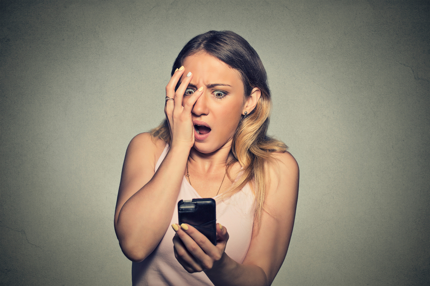 Closeup portrait anxious scared young girl looking at phone seeing bad news photos message with disgusting emotion on her face isolated on gray wall background. Human reaction,