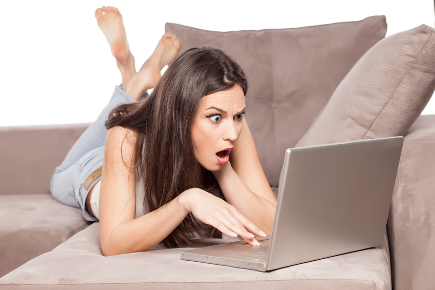 shocked girl lying on the couch and working on her laptop