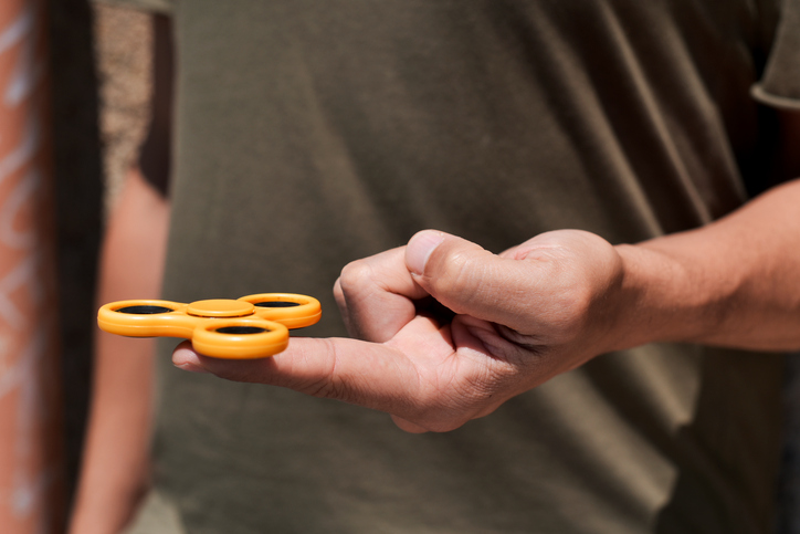 closeup of a young caucasian man playing with a yellow fidget spinner in the street