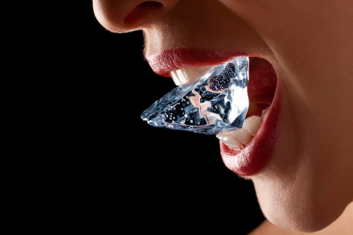 Ice cube in a woman's mouth against black background.