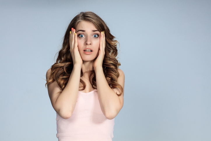 Portrait of young woman with shocked facial expression over gray background