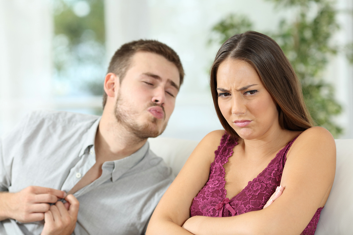 Angry woman rejecting a sex offer from her boyfriend during a date sitting on a couch at home