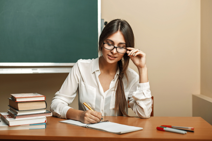 Beautiful young woman with glasses to study at university, reading books and writes in a notebook.