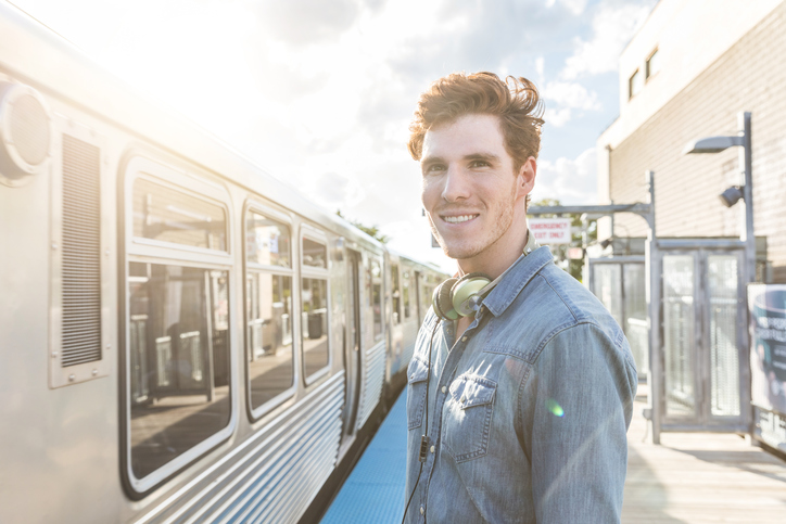 Young man at train or subway station on a sunny day in Chicago. Portrait of a ginger young man looking at camera with a blurred train moving on background.