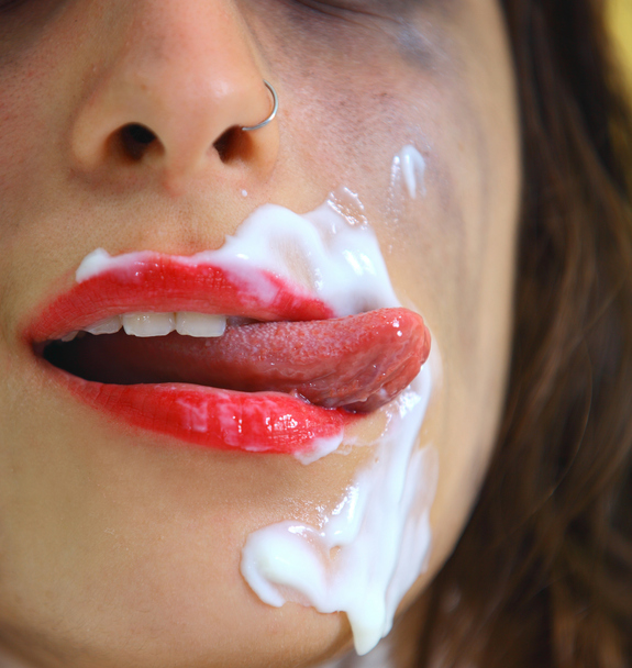 Girl licking her lips covered with white substance, close up
