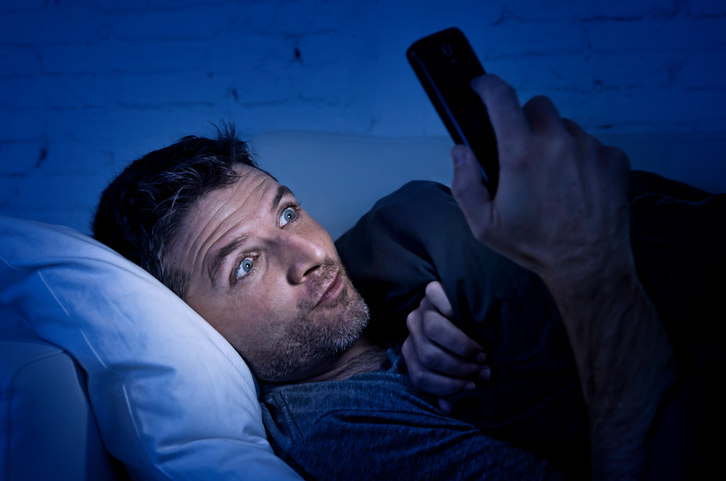 man looking at mobile phone in bed