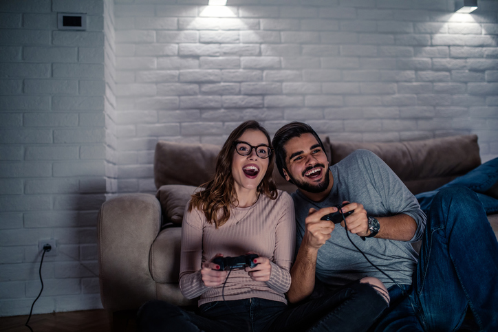Photo of young couple playing video games at home at night.