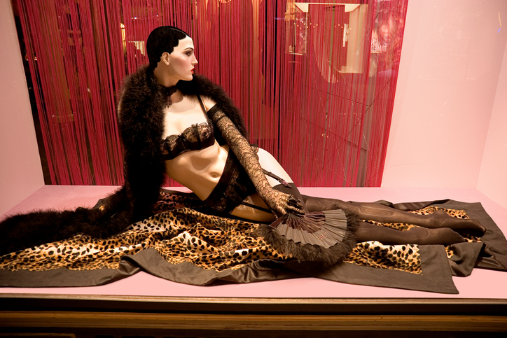 Mannequin in stockings and garter belt lying on fur in a pink window.