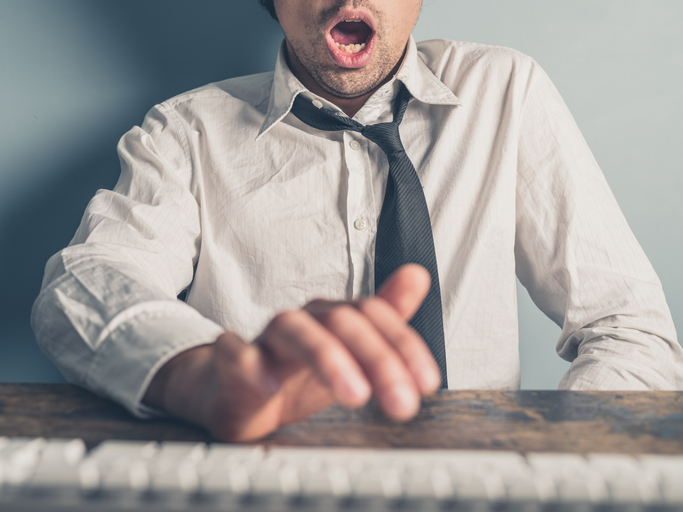 A young businessman is typing on a computer with one hand. His other hand is under the table and he is looking really excited.